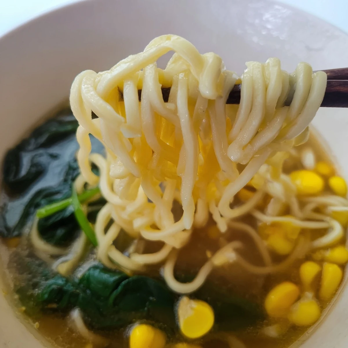 A close-up on Elevated Ramen Egg Drop Soup reveals rich broth, corn, and toasted sesame seeds.