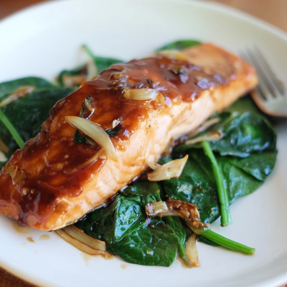 Flaky miso salmon fillet glazed with golden caramelization rests on a bed of bright green sautéed spinach with fresh ginger, served with lemon wedges.