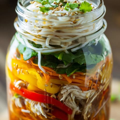 Four Mason Jar Noodle Meal Prep jars sit beside lime wedges and chopped peanuts, ready for shaking.