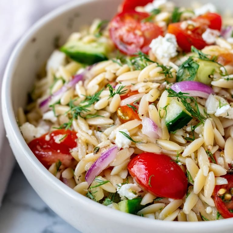 Bright bowl of chilled Greek Orzo Salad, featuring tender pasta, juicy tomatoes, crisp cucumber, and tangy feta cheese, finished with fresh parsley and dill.