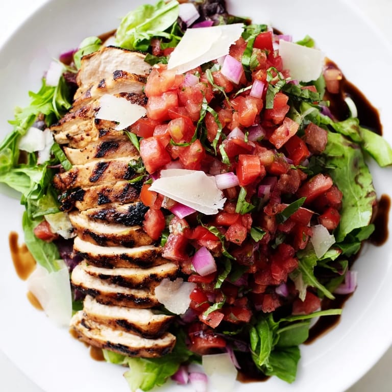 A generous portion of Bruschetta Chicken Salad features tender sliced chicken, fresh tomato-basil topping, and shaved Parmesan on a platter, ready for a summer meal.