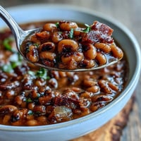 A close-up of a Big Pot of Texas Black-Eyed Peas, garnished with fresh cilantro and green onions, steaming in a rustic Dutch oven.